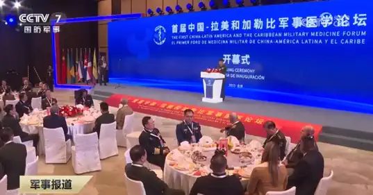 An audience seated at banquet tables listening to a speaker at a lectern on a stage.